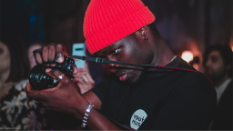 Young person taking a photo wearing a red hat and Youth Music t-shirt