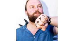 Male with beard holding his fist to the camera, with the words POP! written on his knuckles.