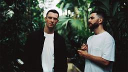 two people in white tshirts with green trees behind them