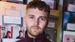 man visible from neck up, blurry posters behind him on the wall