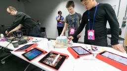 young people wearing lanyards looking down at different Ipads laid out on the table