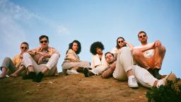 seven people sitting on a grassy hill, blue sky in the background