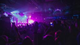 shot of a band playing live, crowd of people with hands in the air, purple and blue lights coming from the stage