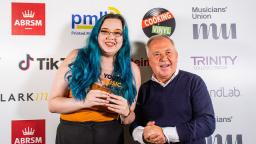 two people, one holding an award, in front of a white wall with logos on it