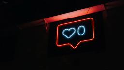 red neon sign shaped like a speech mark, with white heart and circle neon shapes inside it