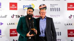 two people standing in front of board with logos, one holding award