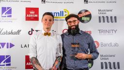 two people standing in front of white board with logos, one holding an award