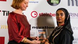 two people standing in front of white board with logos, both holding award between them