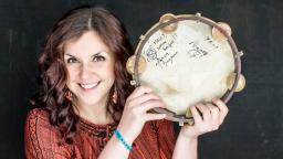 Woman smiling and holding a tambourine next to her face