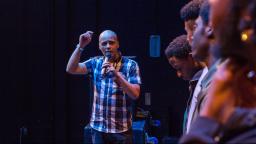 Man in checked shirt speaking into microphone, four young people listening