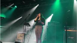 young woman on stage singing into microphone under green lights