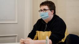 young person wearing a face mask sitting down at a table in a room.