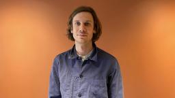 man standing against orange background, visible from waist up