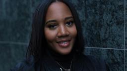 headshot of Shauni, visible from shoulders up, grey brick wall in background