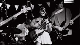 black and white photo of a woman playing guitar on stage with a band