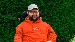 sanjeev mann wears a white cap and a red hoodie with black rimmed glasses