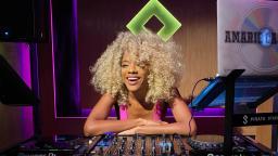 Girl in purple top with blonde hair leaning on DJ decks and laughing