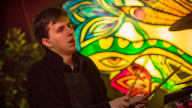 young musician holding drum sticks with a stained glass window behind them