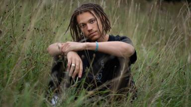 Person wearing all black sitting in a field with their arms resting on their knees.