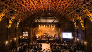 a big room with a stage at the front and lots of people sitting in the audience watching.