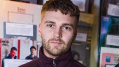 man visible from neck up, blurry posters behind him on the wall