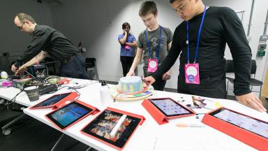 young people wearing lanyards looking down at different Ipads laid out on the table