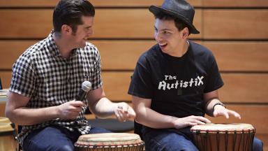 Two people playing standing drums, one wearing a t-shirt reading The Autistix