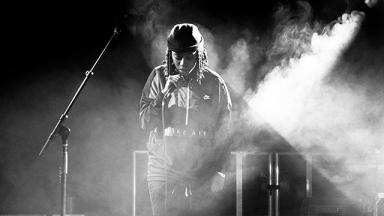 black and white photo of a young person singing on stage with smoke and lights around them