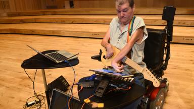 Musician playing adaptive instruments including guitar, keyboard and laptop