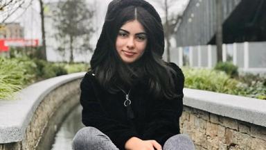 person sitting on a low wall in a black hoody, brick walls visible behind them