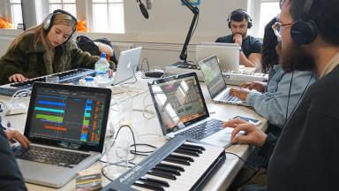 young people sitting around a table on laptops making music