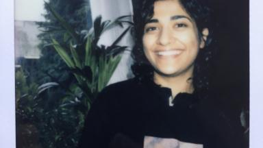 polaroid photo of woman in hoodie standing next to plant