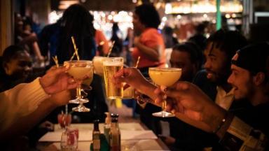 group of people clinking drink glasses together over a table of food