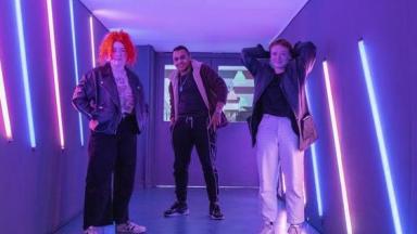 three young people standing in a room lit with purple lights