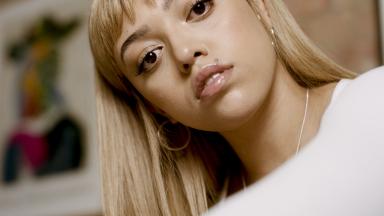 Image of singer-songwriter Mahalia - woman with blonde hair with a fringe wearing a white tshirt.