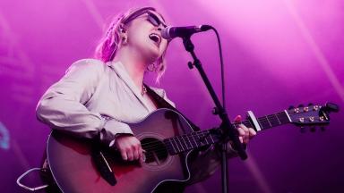 an artist called becharlotte plays the guitar and sings into a microphone