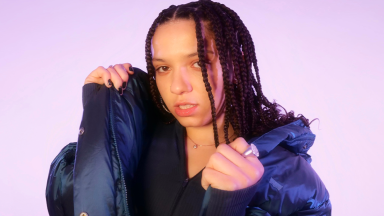 a woman with braids grips the puffer jacket she is wearing