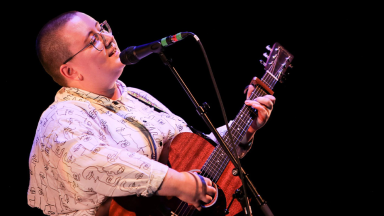 a person with a shaved head sings and plays guitar