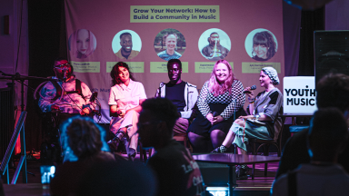 a panel of five people sit on stage in front of an audience