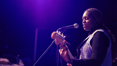 a girl with braids plays electric guitar and sings into a microphone