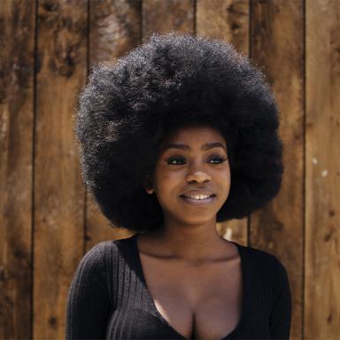 woman smiling wearing a black top standing in front of a wooden panelled wall