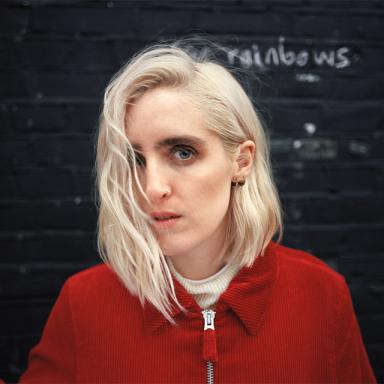 woman with white blonde hair wearing red jacket against black background