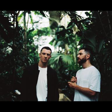 Two men pose for camera with palm trees in background