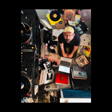 A man surrounded by music records looks up at camera