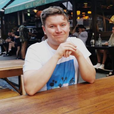 man wearing white t-shirt with blue print on it, sat outside a cafe