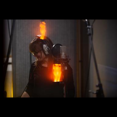 woman standing at mic in a studio booth with lava lamp