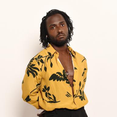 Man with dark hair wears mustard coloured shirt with floral pattern and black jeans