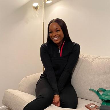 Woman sitting on sofa with dark hair wearing black top and leggings smiles at camera