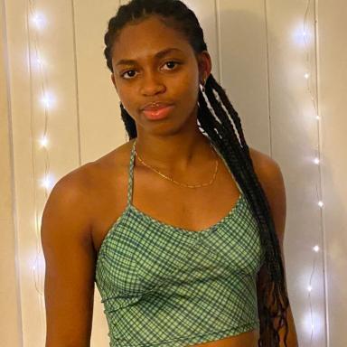 m&i wearing a cropped green vest top, standing in front of a wall of lights