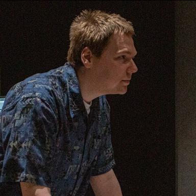 Man with short light brown hair leans on table in music studio